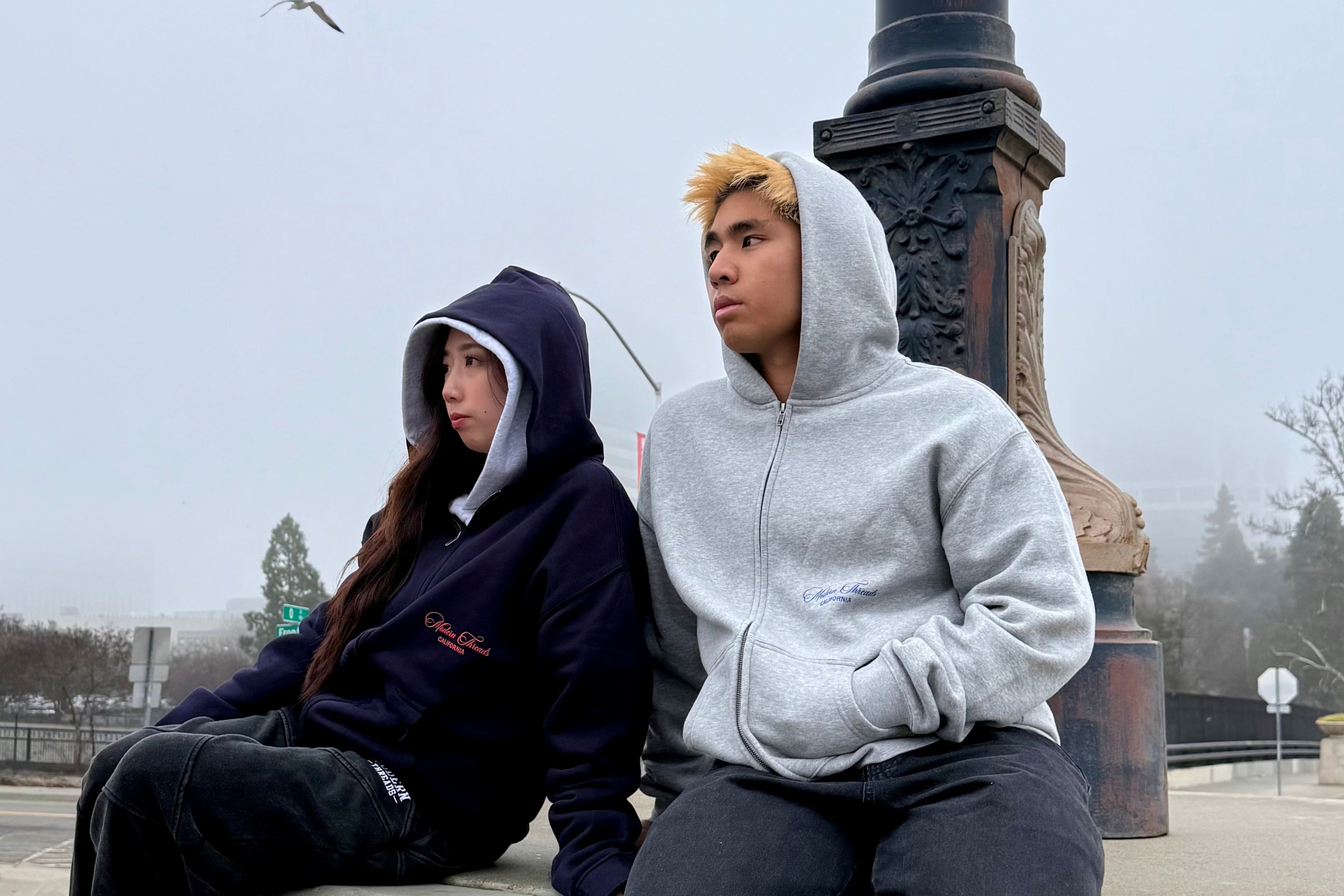 Two people sitting on a ledge with a gloomy sky in the background